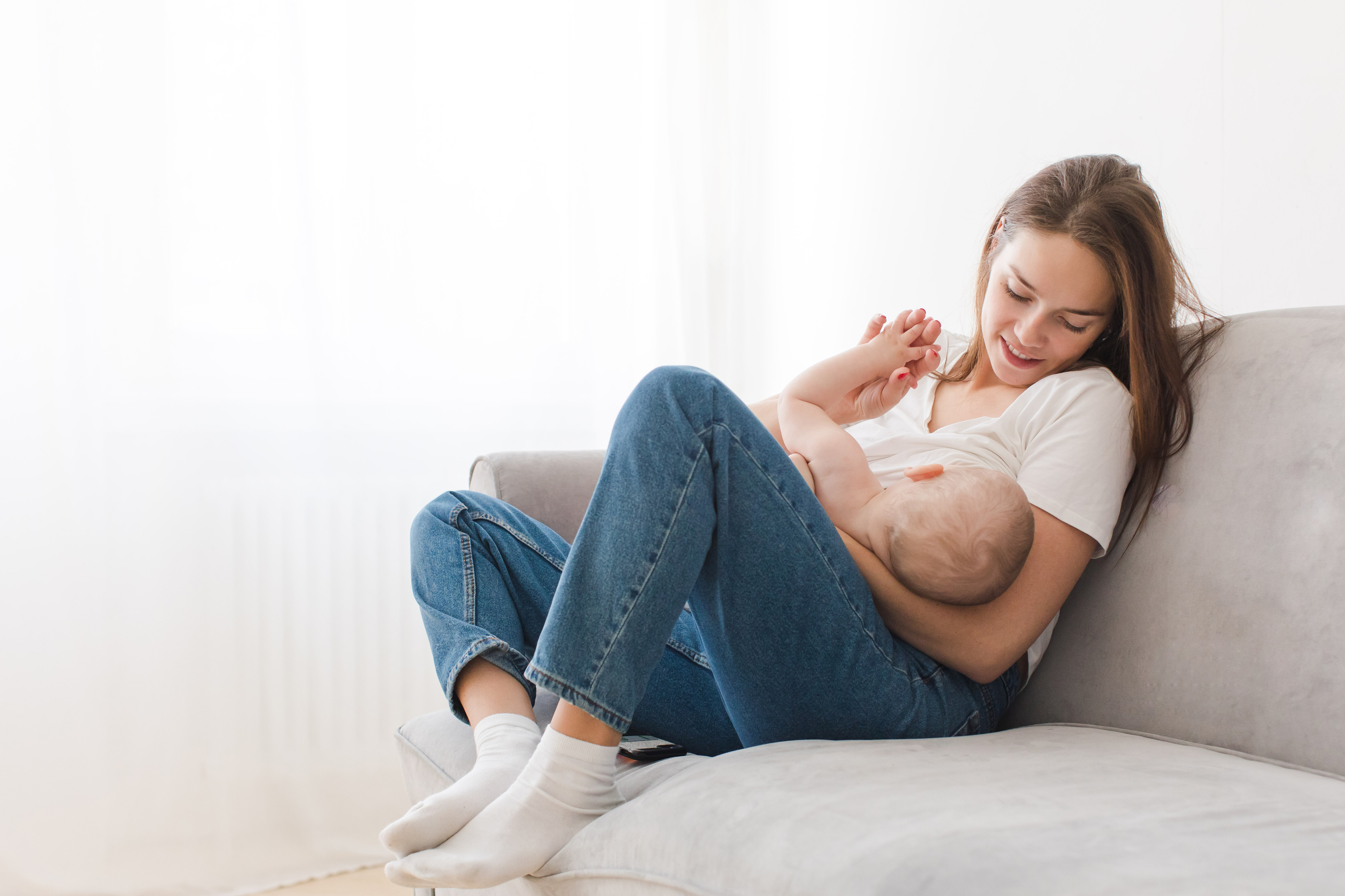 Postpartum woman sitting on the couch breastfeeding her newborn baby