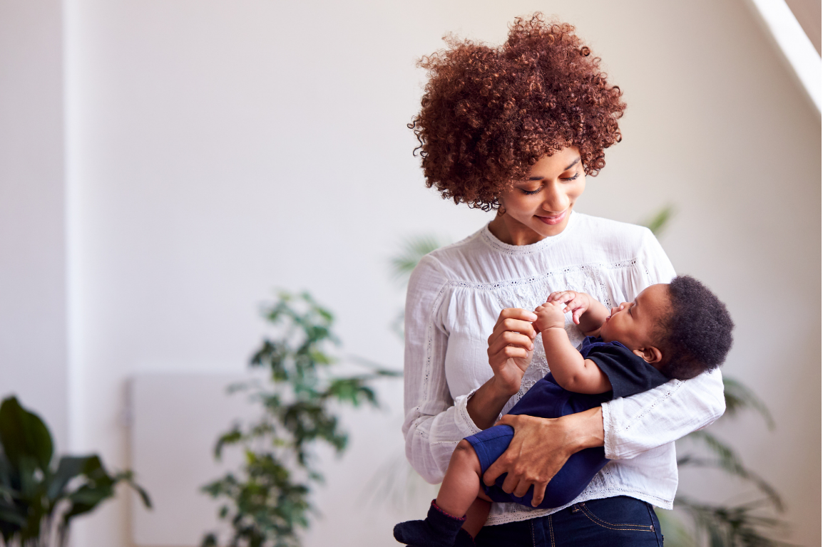 Black woman holding baby looking at him lovingly, both well rested with the help of a postpartum doula